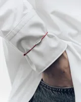 Pulsera de cordón rojo con un dije central plateado de diseño orgánico y grabado de la marca.
