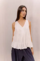 Musculosa blanca de diseño holgado con escote en V, costuras decorativas frontales, tablas encontradas en el centro y un delicado volado en el ruedo.
