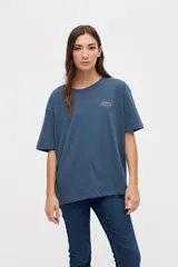 Remera de manga corta color azul, con calce clásico y tajos laterales. Presenta un bordado pequeño en el pecho con el texto 'UNIFORM STUDIO LAB' y un detalle bordado en la manga. Confeccionada en algodón lavado con textura suave.