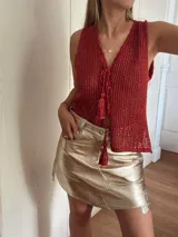 Chaleco tejido en punto calado con hilo de algodón y lurex, de color negro con destellos plateados. Presenta escote profundo en V, cierre frontal con cordones entrelazados terminados en borlas y un corte recto y holgado.