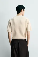 Camiseta regular fit de punto tejido en hilatura de algodón de color beige, con cuello redondo y cierre frontal de botonadura tipo panadero, manga corta y acabados en rib.