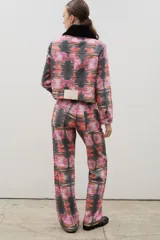 Pantalón de tiro alto confeccionado en denim de corte recto, con estampado artístico abstracto en tonos rosados, rojos y negros. Presenta cierre frontal con botones visibles.