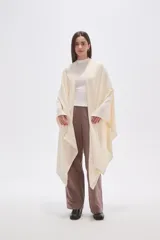 Poncho abierto color crudo, de diseño holgado y caída fluida.