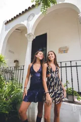 Vestido corto negro con estampado de plumas doradas, escote en V, breteles finos cruzados en la espalda, cut-outs laterales y volado en el ruedo.