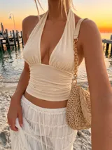 Top halter de color beige con escote pronunciado, tirantes anudados al cuello y diseño fruncido en el cuerpo.