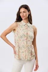Camisa sin mangas de lino y algodón, con estampado floral en tonos violeta y verde sobre base beige, cuello camisero y cierre frontal de botones.