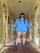 Buzo deportivo de color azul claro, estilo oversize, con cuello redondo y puños y ruedo con elástico. Presenta un pequeño logo bordado en el pecho.