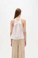 Top blanco de algodón con cuello halter, diseño holgado y detalle de encaje en el borde inferior.