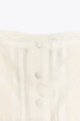 Top blanco de escote recto y tirantes finos ajustables, con detalle de lazos a contraste y flores bordadas. Cierre frontal con botones forrados en el mismo tejido.