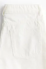 Short de denim de algodón rígido, color blanco, de tiro alto con cinco bolsillos, cierre de cremallera con botón y terminación deshilachada en el bajo.