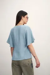 Camisa negra con botones dorados, escote en V y mangas cortas amplias con lazos laterales. 