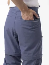 Pantalón Merrell desmontable de trekking color gris, de corte recto y tiro medio, confeccionado con tejido elástico de poliéster y spandex. Incluye cinturón ajustable, bolsillos laterales con cierre y logo reflectante.