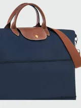 Bolso de viaje ampliable Longchamp modelo Le Pliage Original, color azul marino. Presenta diseño minimalista con asas cortas y correa larga ajustable en color marrón, cierre superior con solapa de cuero y botón a presión metálico.
