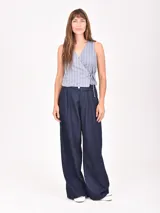 Chaleco sin mangas de color beige con rayas verticales blancas. Presenta un diseño cruzado tipo wrap con escote en V y ajuste mediante lazo lateral.