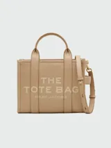 Cartera tipo tote de Marc Jacobs, confeccionada en cuero granulado color azul marino. Presenta el logo de la marca estampado en el frente, doble asa superior y correa ajustable y extraíble para llevar al hombro o cruzada.