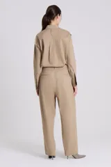 Pantalón sastre de corte recto en tejido plano de algodón color beige, con detalle de solapa asimétrica en la parte superior izquierda.