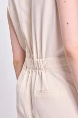 Mono largo color crudo de lino, con cuello en V, sin mangas, corte a la cintura con botón y pantalón de corte recto.