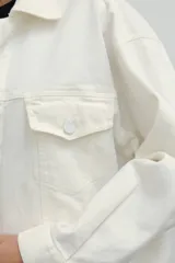 Campera de jean color crudo, con cuello camisero, cierre frontal con botones y bolsillos con solapa en el pecho.