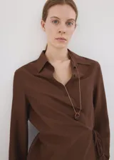 Camisa cruzada de color marrón, con diseño recto, cuello camisero, manga larga y cierre de lazo en la cintura con botones.