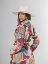 Trench de diseño urbano con acabado agamuzado, de corte recto y largo midi. Presenta un estampado abstracto multicolor con tonos rojizos, azules y ocres, cuello solapa, mangas largas y cinturón ajustable en la cintura.