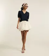 Minifalda blanca de poliéster, corte baloné, con elástico y lazo ajustable en la cintura.