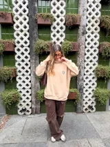 Buzo tipo hoodie color crudo, de calce oversize, con cuello alto y estampa pequeña de una carita sonriente azul en el pecho.