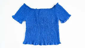 Top de color azul con diseño fruncido en toda la prenda, escote estilo hombros caídos y mangas cortas con terminación de volados.