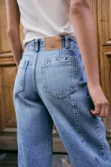 Jeans de tiro alto con corte barrel, pernera holgada que se estrecha hacia el tobillo y bajo deshilachado. Presenta costuras verticales decorativas en el frente y cierre frontal con cremallera y botón.