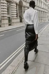 Camisa de cuello solapa y manga larga, con estampado de rayas verticales blancas y grises. Presenta dos aplicaciones de flores de encaje negro en la parte frontal. Cierre frontal con botones ocultos por solapa.