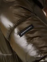 Campera puffer larga de abrigo marca BCBG Maxazria, color beige. Cuenta con capucha desmontable, cuello alto envolvente, cierre frontal bidireccional con solapa de botones a presión, bolsillos laterales, puños internos elastizados y tajos laterales con cierre en el bajo.