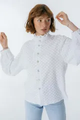 Camisa blanca con textura, cuello alto con volados y cierre frontal con botones.