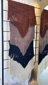 Ruana tejida a mano en lana merino, de color negro, con diseño de textura tejida y terminaciones con flecos largos en todo el borde.