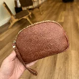 Monedero de cuero color marrón con cierre dorado y correa de mano.