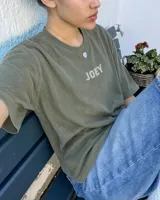 Remera oversize gris oscuro con corte holgado, mangas cortas y estampa trasera en blanco y negro con forma de estampilla que muestra a una persona con un gato y el texto 'Kaboa Industries'.