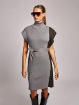 Vestido midi de tejido de punto acanalado, con cuello alto y diseño bicolor que combina gris claro en el frente y verde oscuro en el lateral. Presenta mangas cortas tipo sisa y un lazo ajustable en la cintura del mismo tejido.