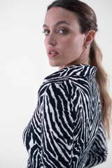 Vestido midi de corte ajustado, con estampado animal print tipo cebra en blanco y negro, cuello camisero, escote en V y cierre frontal con botones dorados.