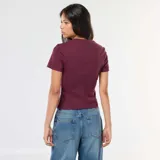 Remera de punto de canalé color borgoña, de corte ajustado, con cuello redondo y mangas cortas. Presenta una costura vertical central en el frente y una pequeña abertura en el ruedo.