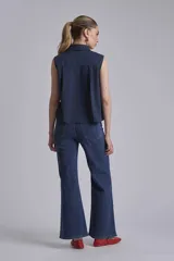 Camisa azul marino sin mangas con cuello clásico, abotonada al frente y detalle de plisados verticales en el pecho.