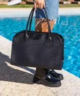 Bolso tipo tote de cuero negro con textura tipo piel de cocodrilo, doble asa de mano y cierre superior con cremallera.