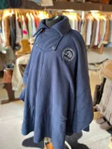 Poncho polar azul marino con cuello alto, solapa frontal con botones y bordado circular del equipo Criollos en el pecho.