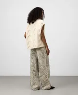 Chaleco de punto color crema, con cuello chimenea y diseño de ochos trenzados. Presenta mangas sisa con hombro caído.