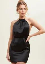 Vestido corto de satén color negro, con escote halter y detalle de cadena metálica en el cuello. Presenta un diseño sin mangas con espalda descubierta y ajuste en la cintura.