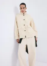 Chaqueta de algodón estilo denim, de diseño oversize, color beige, con cuello alto, manga larga, bolsillos de parche con solapa y cierre frontal de botones oscuros.