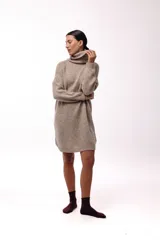 Vestido de punto color beige, de corte holgado y diseño oversized, con cuello alto tipo polera y mangas largas.
