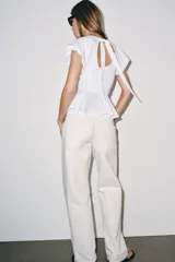 Top de popelina blanca con cuello redondo, mangas cortas abullonadas y detalle de abertura en la espalda con lazada. Presenta bajo en evasé tipo peplum y cierre lateral con cremallera oculta.