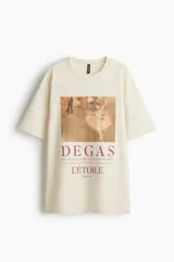 Remera oversized de algodón color beige, de manga corta con hombros caídos y cuello redondo ribeteado. Presenta un estampado frontal con la obra de Edgar Degas "L'Étoile" y texto en tonos bordo.