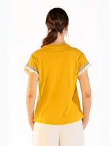 Remera color naranja de manga corta, confeccionada en algodón, con detalles de flecos y bordado en las mangas.