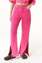 Pantalón de jean fucsia de pierna ancha con corte lateral acordonado en el bajo y detalle de tela roja en el lateral.