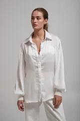 Camisa blanca de mangas largas abullonadas con puños elásticos, cuello clásico y cierre frontal con botones.