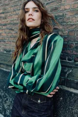 Camisa de manga larga con escote fluido tipo pañuelo, hombreras y puños abotonados. Presenta un diseño de rayas verticales en tonos verdes y amarillos.